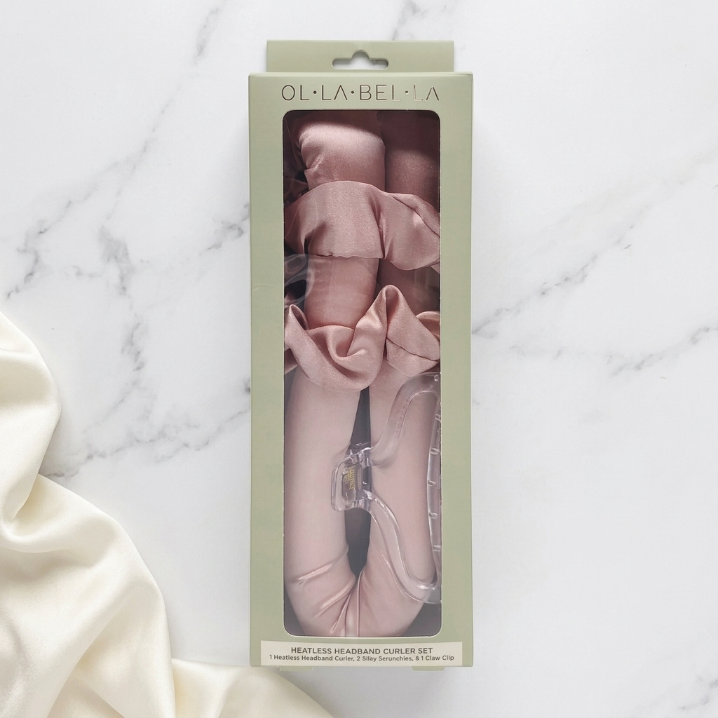 Olla Bella Heatless Curling Heatband kit in its light sage green packaging, displayed on a white marble surface with a cream fabric prop.