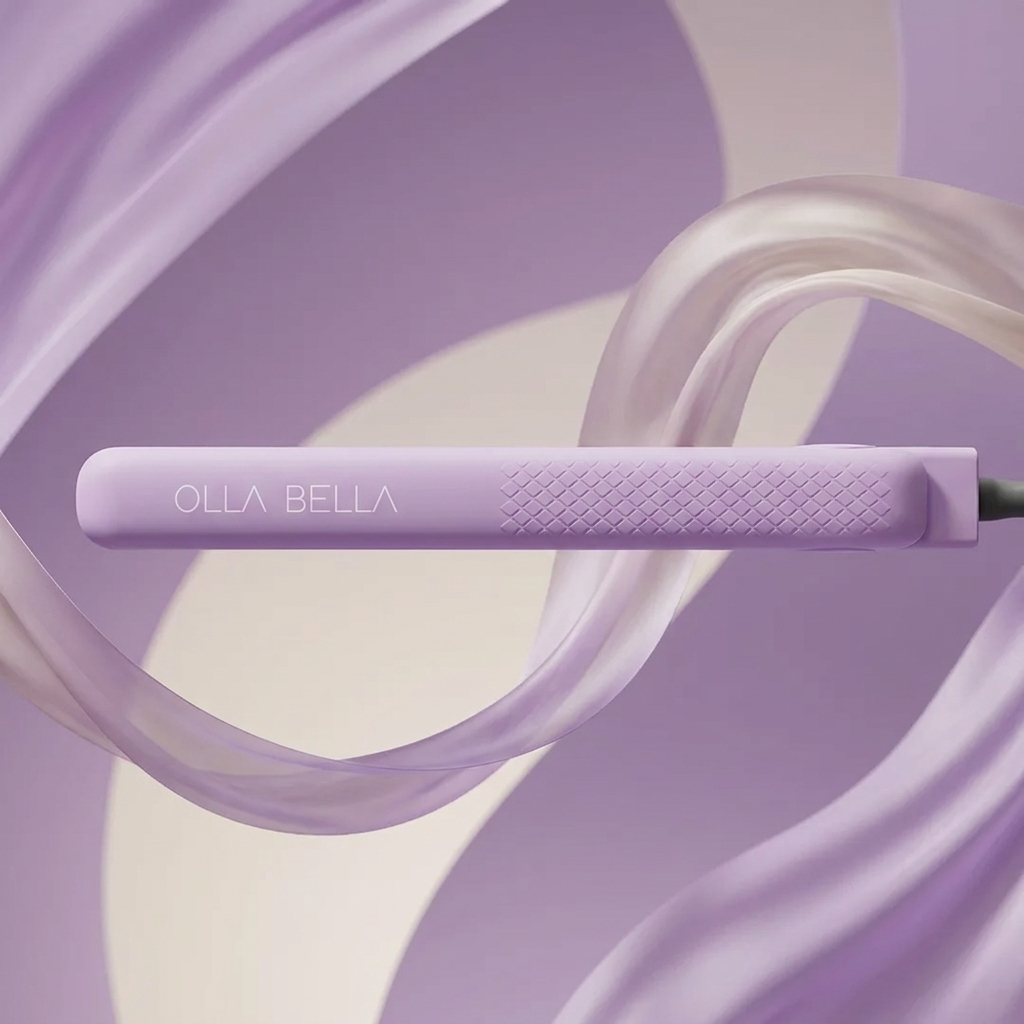 A Lilac You A Lot Olla Bella 1.25" Ceramic Hair Straightener shown horizontally against a stylized background of flowing translucent lavender and cream ribbons.