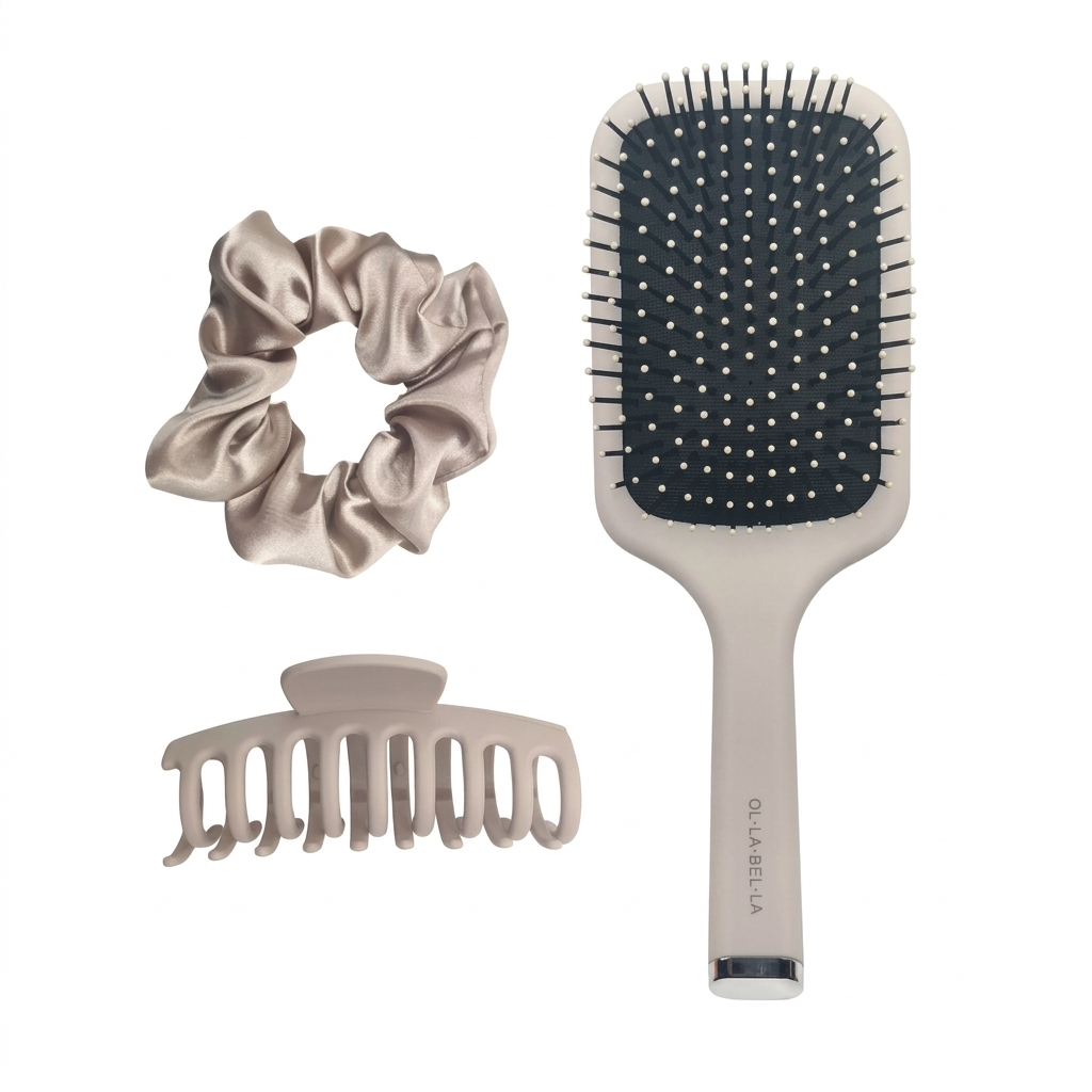 The Olla Bella Everyday Glam Hair Accessory Kit featuring a satin scrunchie, a claw clip, and a paddle brush in a matching light beige color, arranged on a solid white background.
