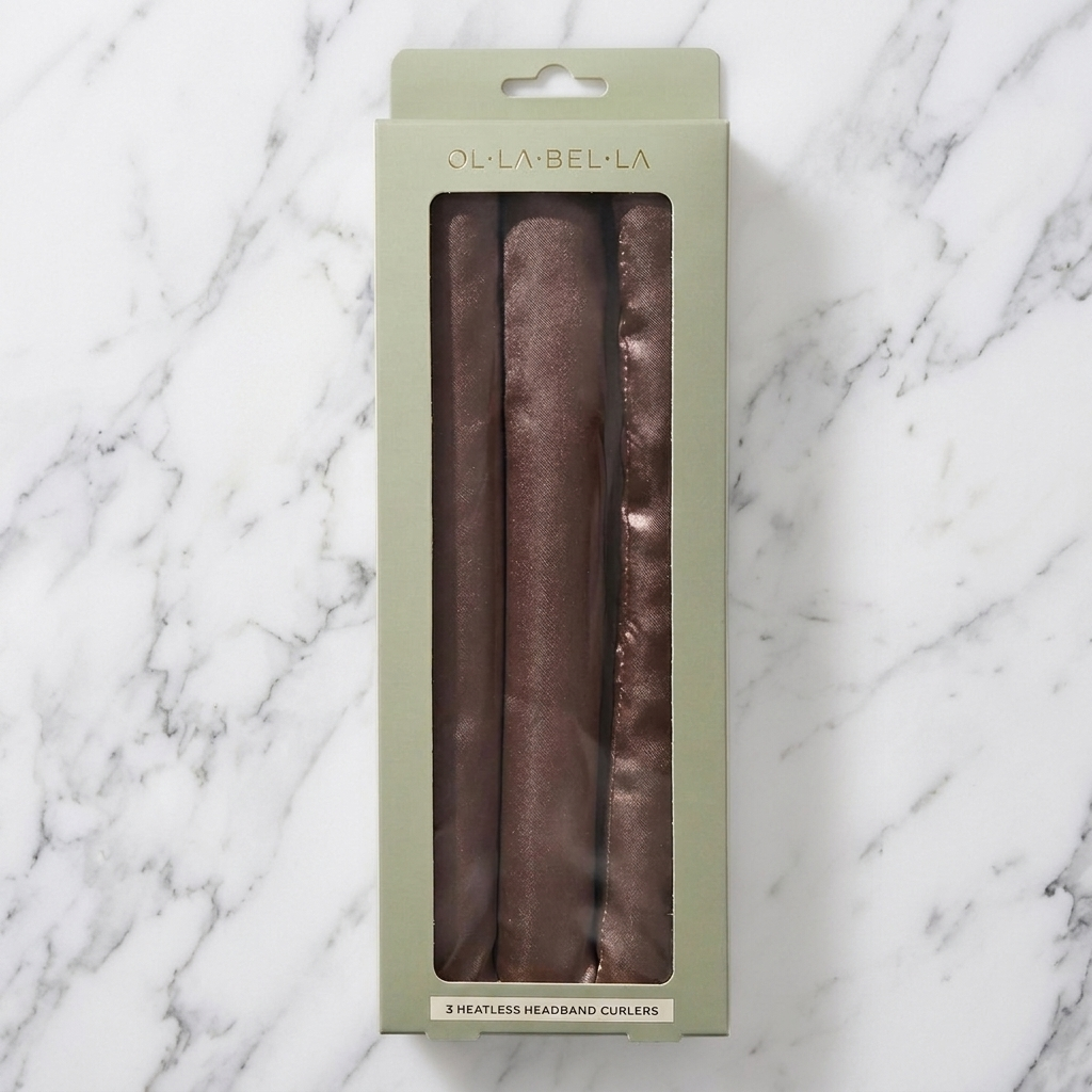 A package of three Olla Bella Jumbo Heatless Curler Rods, shown in a light sage green box with a clear window, set against a white marble background.