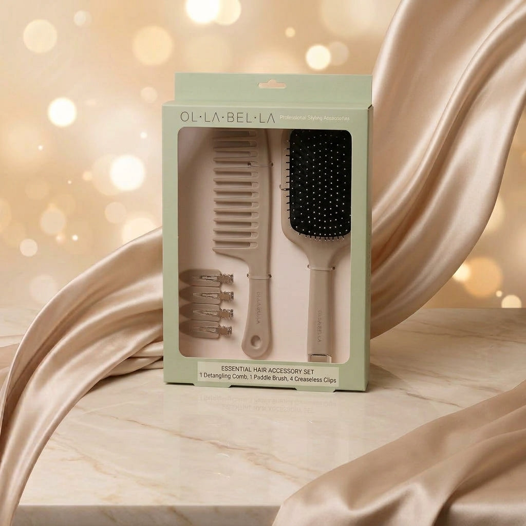 The Olla Bella Knot Today Detangling Brush Kit in its original packaging, featuring a detangle brush, paddle brush, and four creaseless sectioning clips, styled with draped champagne satin fabric and a warm bokeh background.