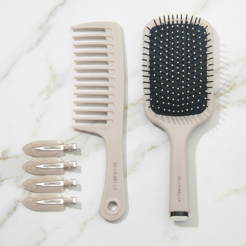 The Olla Bella Knot Today Detangling Brush Kit featuring a detangle brush, a paddle hairbrush, and four creaseless sectioning clips, all in a light beige color on a marble background.