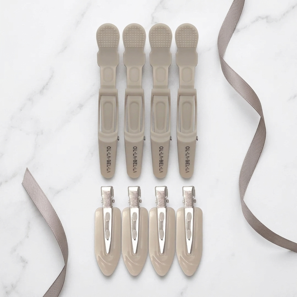 Four Olla Bella Crocodile Clips and four Olla Bella Creaseless Clips from our Olla Bella Mane Master Hair Clip Set arranged in two rows of two on a light marble background with ribbons.