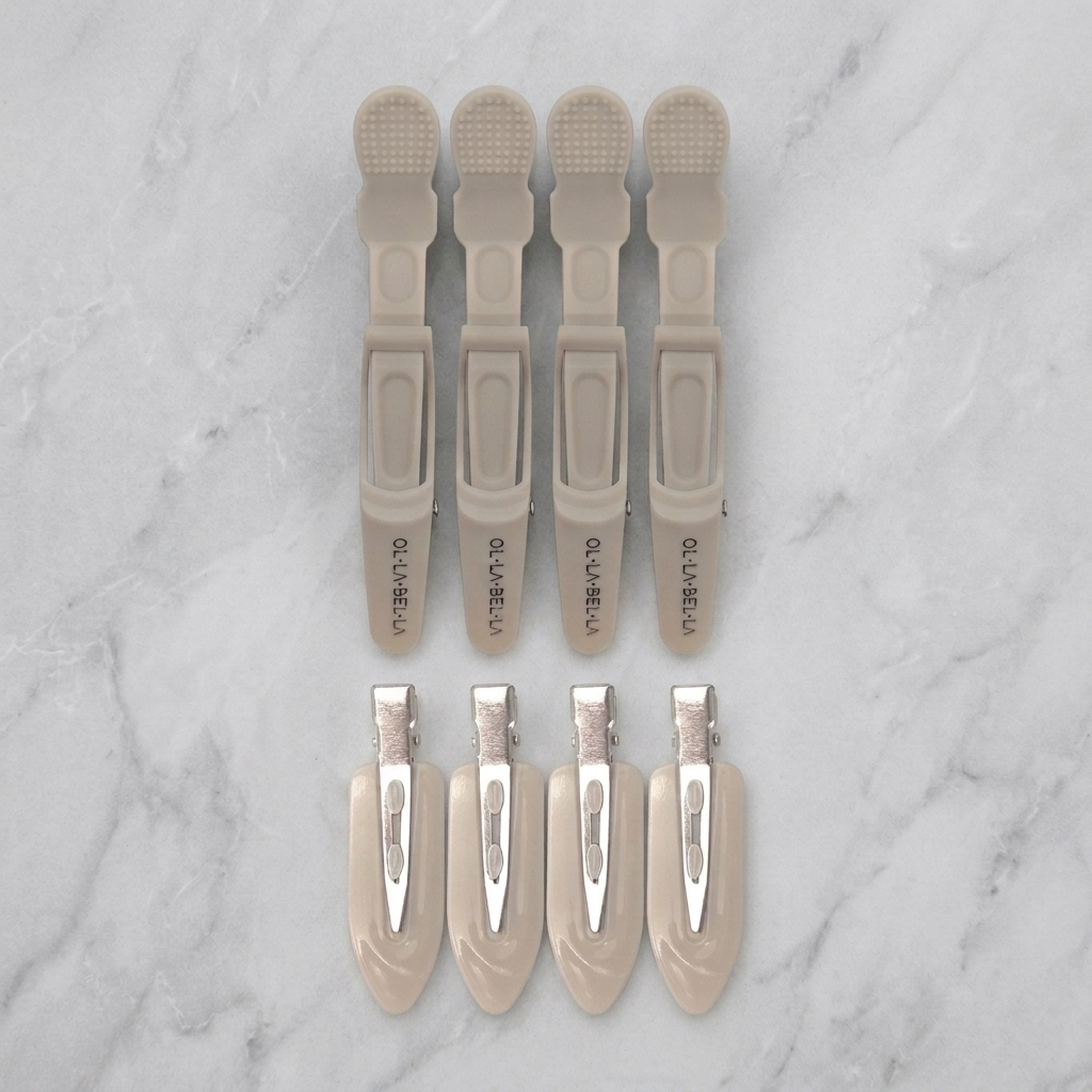 Four Olla Bella Crocodile Clips and four Olla Bella Creaseless Clips from the Olla Bella Mane Master Hair Clip Set arranged in two rows of two on a marble background.