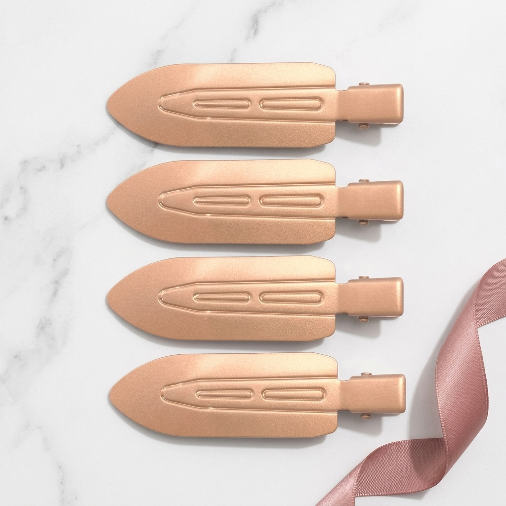 Four Olla Bella No-Crease Cuties - Creaseless Hair Clips arranged vertically on a white marble background with a pink ribbon in the bottom right corner.