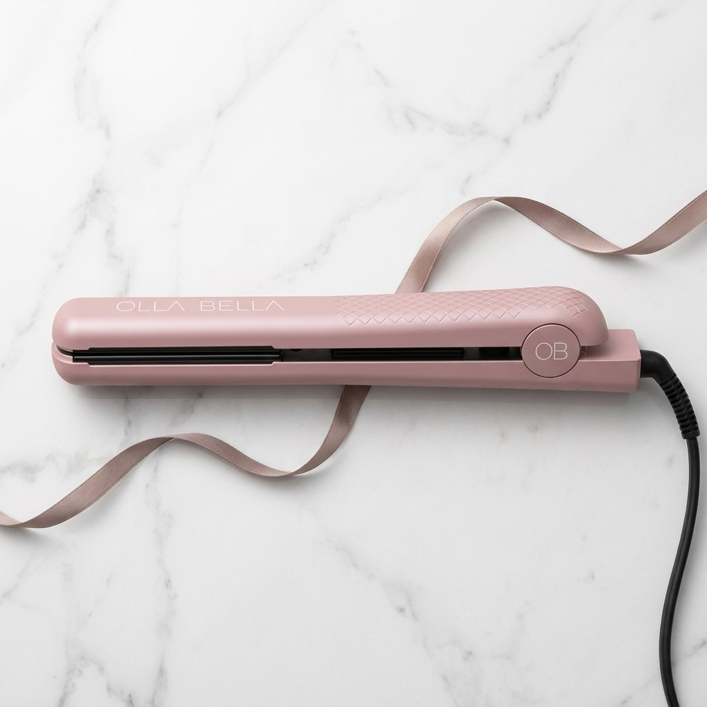 A Blush Pink Metallic Olla Bella 1.25" Ceramic Hair Straightener with a matching ribbon accessory, displayed on a white marble background.