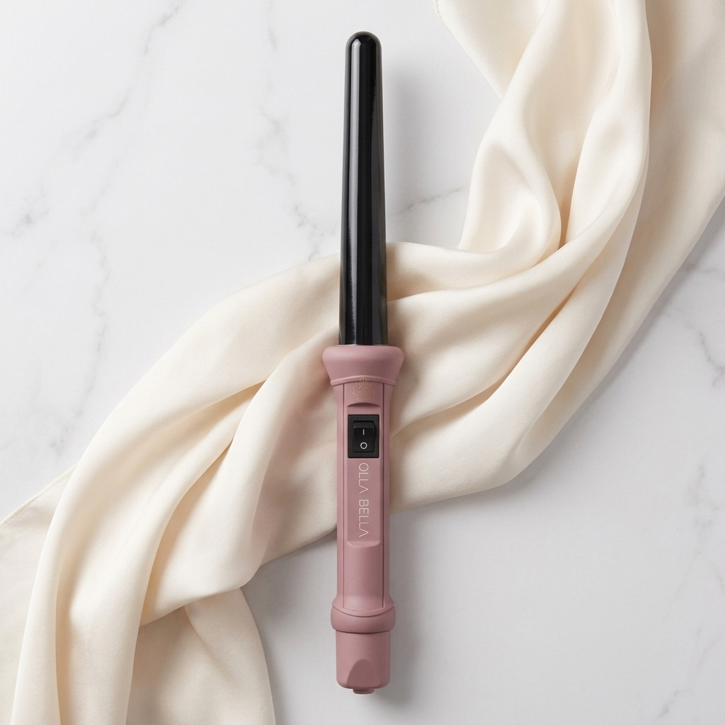 The Olla Bella 1" Ceramic Curling Iron in Ballet Pink styled on a white marble surface with draped cream-colored satin fabric.